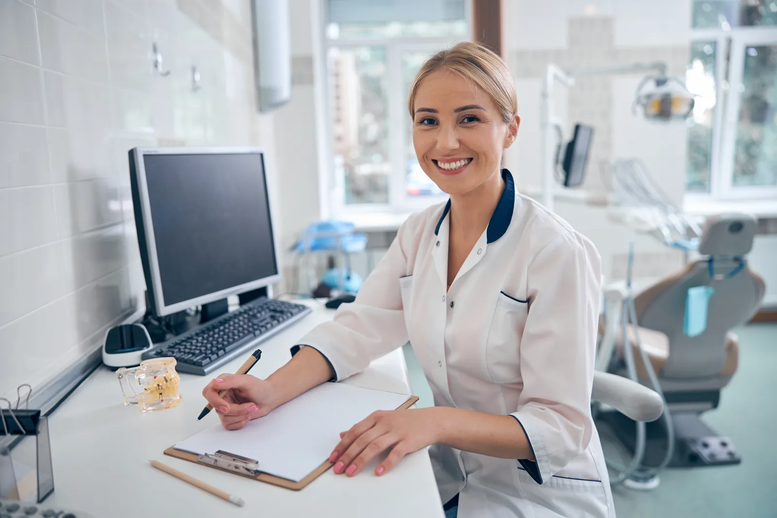 A dentist at the practice desk, working through paperwork beside the operatory